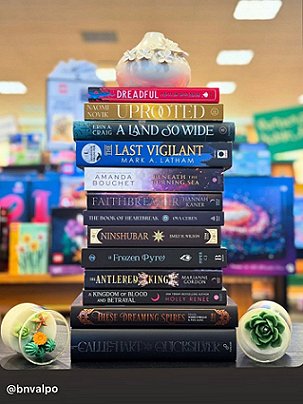 screenshot from @bnvalpo showing a stack of hardback books on a dark wooden shelf. Second from the bottom is a copy of These Dreaming Spires, edited by Marie O'Regan and Paul Kane