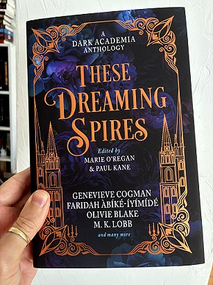 photograph showing a man's hand holding a copy of These Dreaming Spires, edited by Marie O'Regan and Paul Kane, against a white background