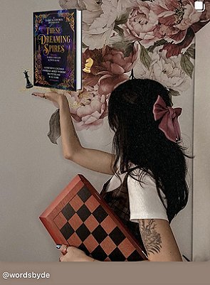 photograph of author De Elizabeth standing side on to the camera, holding up a copy of These Dreaming Spires edited by Marie O'Regan and Paul Kane. In her left hand is a pink and black folded chessboard.