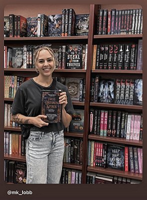 photograph of a smiling M K Lobb in a bookstore, holding a copy of These Dreaming Spires, edited by Marie O'Regan and Paul Kane