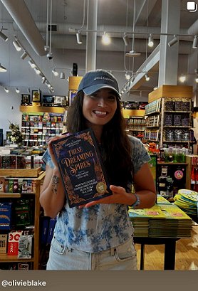 photograph of a smiling Olivie Blake standing in a bookstore, holding a copy of These Dreaming Spires, edited by Marie O'Regan and Paul Kane