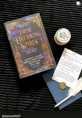 photograph of a copy of These Dreaming Spires, edited by Marie O'Regan and Paul Kane, lying on a black cloth. To the right of hte book are a jar candle with In These Hallowed Halls written on the lid, a note and a coin lying on a blue envelope and a white quill pen