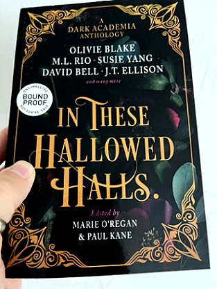 A hand holding an advanced review copy of In These Hallowed Halls, edited by Marie O'Regan and Paul Kane