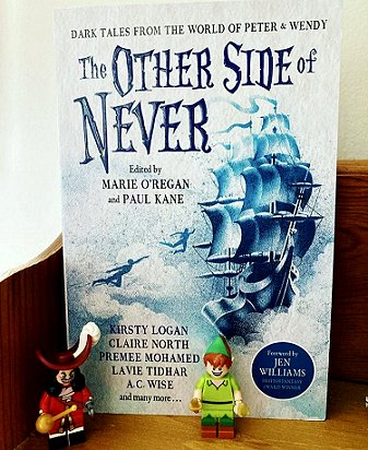 photograph of a copy of The Other Side of Never, edited by Marie O'Regan and Paul Kane, standing on a wooden surface. In front are Lego figures of Captain Hook on the left, and Peter Pan on the right