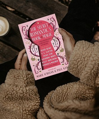 photograph showing a woman in a fawn fleece jacket holding a copy of The Secret Romantic's Book of Magic, edited by Marie O'Regan and Paul Kane