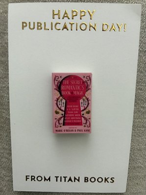pin of the cover of The Secret Romantic's Book of Magic, edited by Marie O'Regan, on white card. Text reads HAPPY PUBLICATION DAY! FROM TITAN BOOKS