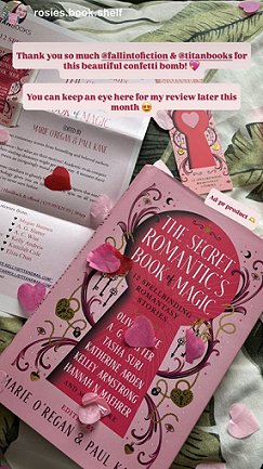 image showing a copy of The Secret Romantic's Book of Magic, edited by Marie O'Regan and Paul Kane, lying on a white cloth decorated with green leaves, alongside a copy of the press release for the book, a Secret Romantic's bookmark, and pink heartshaped confetti