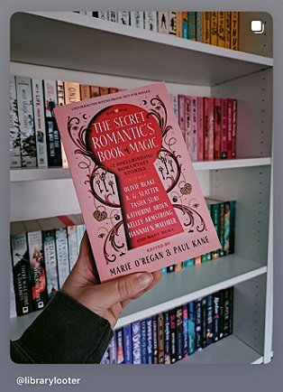 photogrpah of a hand holding a copy of The Secret Romantic's Book of Magic up against a full white bookcase