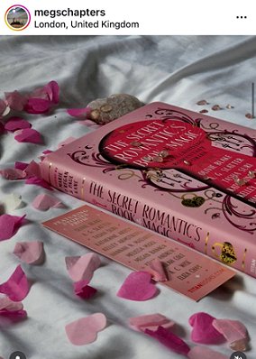 photograph of a copy of The Secret Romantic's Book of Magic, edited by Marie O'Regan and Paul Kane, lying on a white cloth surrounded by pink heartshaped confetti and a Secret Romantic's bookmark is to the left of the book