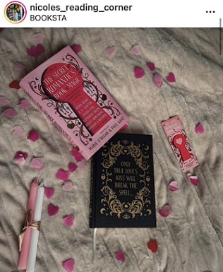 photograph showing a copy of The Secret Romantic's Book of Magic, edited by Marie O'Regan and Paul Kane, lying on a cream cloth scattered with pink heartshaped confetti. To the left is a pink candle and a white candle, tied with gold ribbon, to the right is a Secret Romantic's bookmark. The book itself is lying next to its dustjacket, to show the black cover decorated with gold scrollwork surrounding the text: ONLY TRUE LOVE'S KILL WILL BREAK THE SPELL...